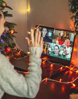 Remote employee taking part in a virtual Christmas event on a video call with festive decorations and team members on screen