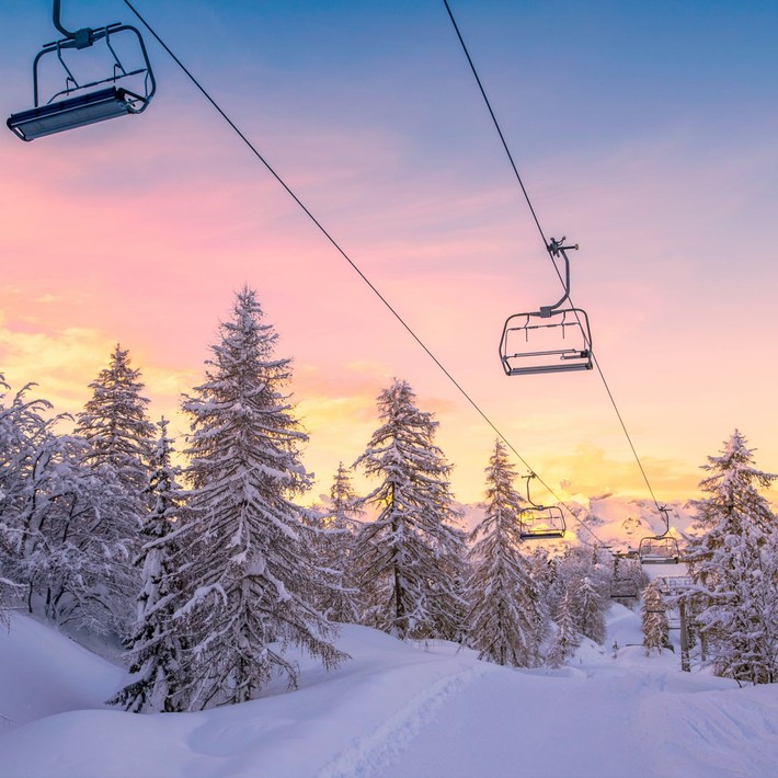 Snowy ski lift at sunrise surrounded by pine trees, representing the winter setting of the Murder on the Slopes virtual team building game in Ireland.
