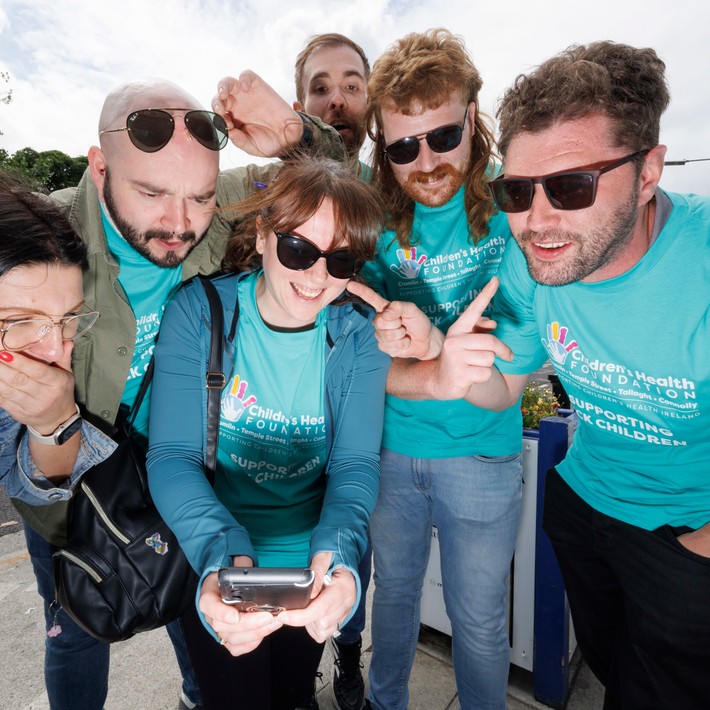 Team of six smiling and pointing at a smartphone screen during a digital treasure hunt