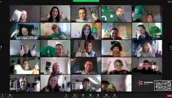 A vibrant virtual St. Patrick’s Day event featuring a multinational corporate team on a video call. Participants are dressed in festive green attire, holding Irish-themed props, and giving thumbs-up, creating an engaging and celebratory atmosphere. The Dynamic Events logo is visible, reinforcing the corporate virtual team-building theme.