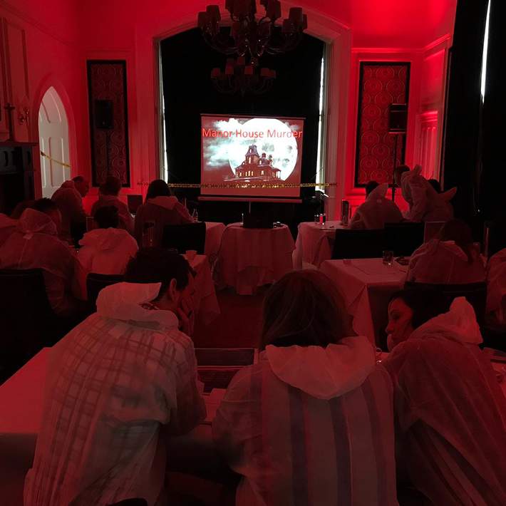 A dramatic, red-lit room filled with corporate teams in forensic-style coveralls, collaborating to analyse evidence and crack the case. The high-energy setting encourages teamwork, communication, and problem-solving in a fun, engaging way.