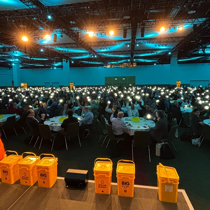 Corporate team in Ireland taking part in a SolarBuddy CSR team building event, holding assembled solar lights during the Hour of Power activity in a large conference venue.
